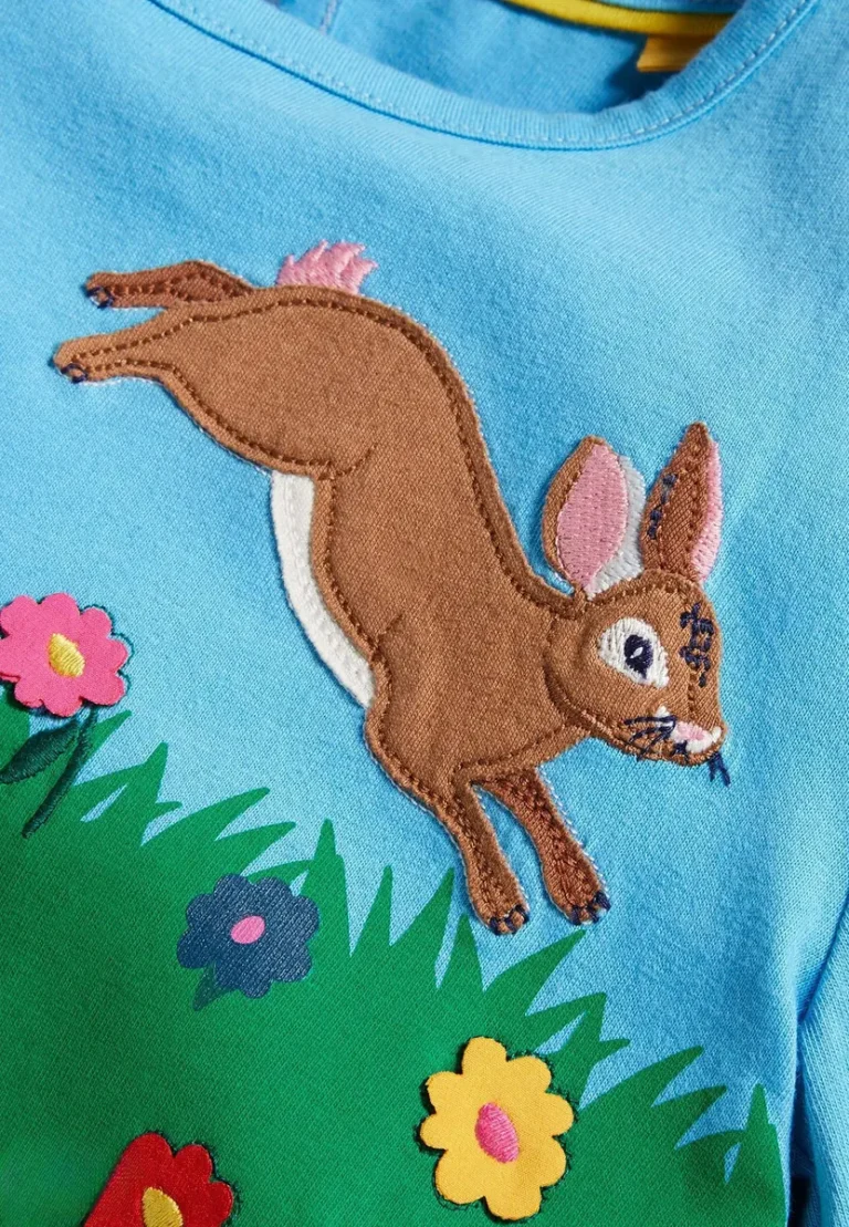 Appliqué brown hare leaping over grass and flowers on a blue kids T-shirt