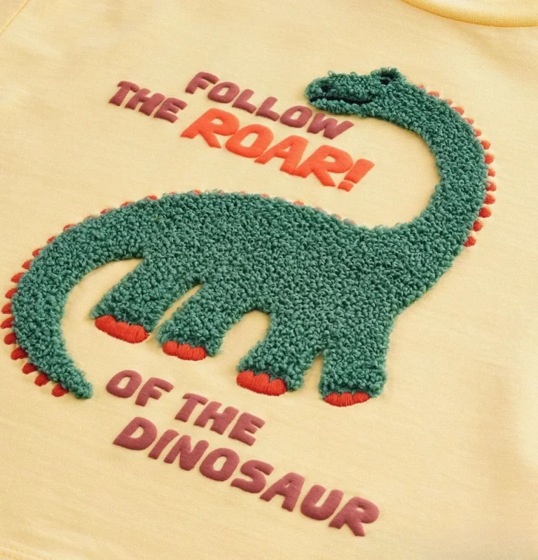 Green chenille dinosaur with printed slogan on a yellow kids T-shirt