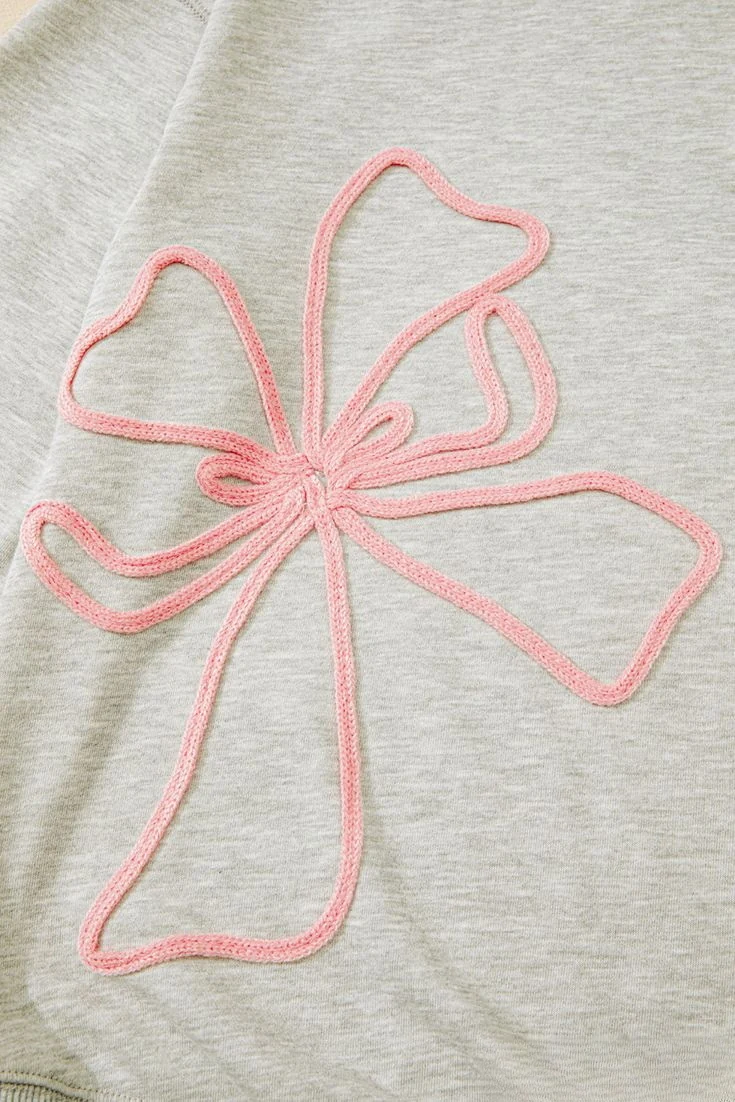 Pink cord embroidery forming a bow on a light grey sweatshirt