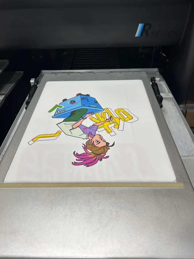 White T-shirt on the platen of a direct-to-garment printer with a full-color cartoon print