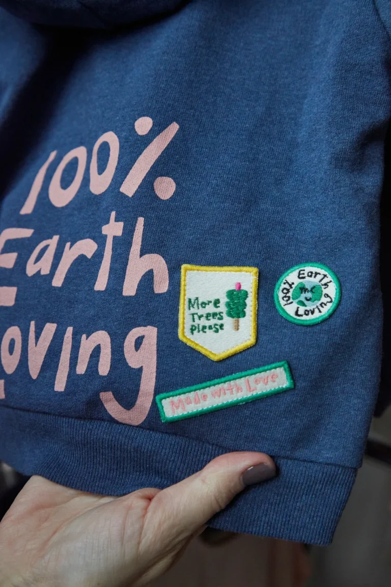 Small embroidered badges beside '100% Earth Loving' print on a navy kids sweatshirt