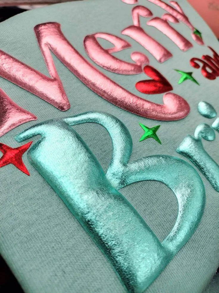 Metallic pink and teal puff-printed holiday lettering on a sweatshirt